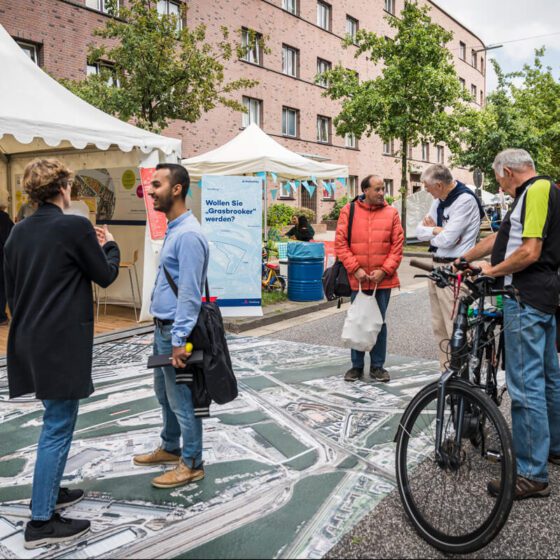 Fußgänger und Fahrradfahrer stehen vor einem Info-Pavillon zum Stadtteil Grasbrook.